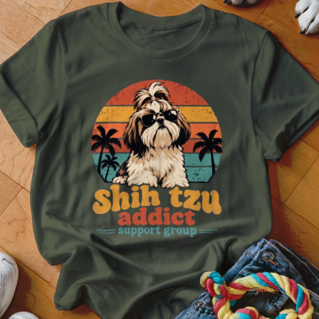 An olive green t-shirt featuring a retro graphic of a Shih Tzu wearing sunglasses against a sunset and palm tree background, with the text Shih Tzu Addict Support Group.