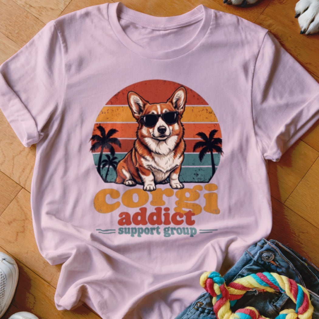 Light pink t-shirt featuring a retro graphic of a corgi wearing sunglasses before palm trees and a sunset.