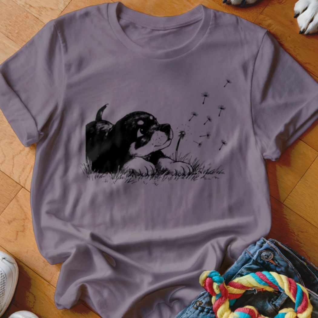 A grey t-shirt featuring a graphic print of a puppy looking at blowing dandelion seeds.