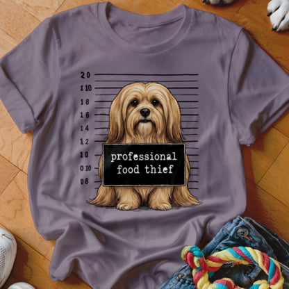 Brown dog in mugshot with sign "professional food thief" on a t-shirt.