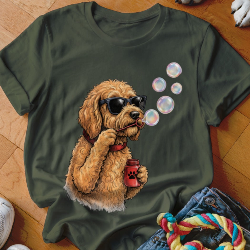 An olive green t-shirt features a graphic of a fluffy, golden dog wearing sunglasses and blowing soap bubbles.