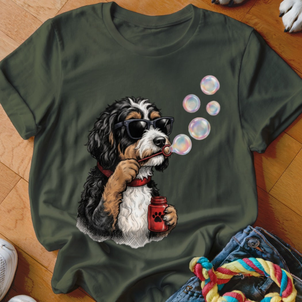An olive green crewneck t-shirt featuring a graphic of a Bernedoodle wearing sunglasses and blowing soap bubbles.