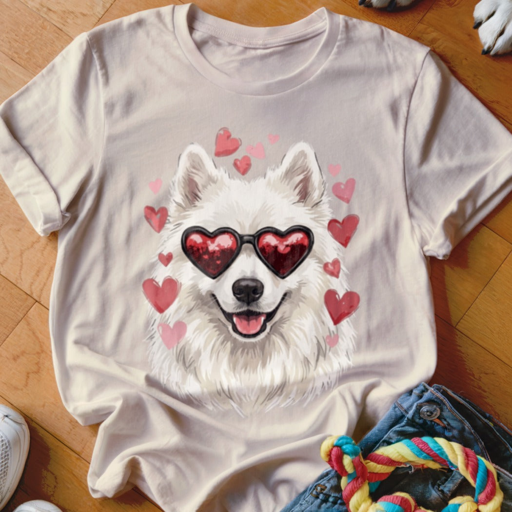 A light pink t-shirt displays an illustration of a white dog wearing heart-shaped sunglasses surrounded by floating pink hearts.
