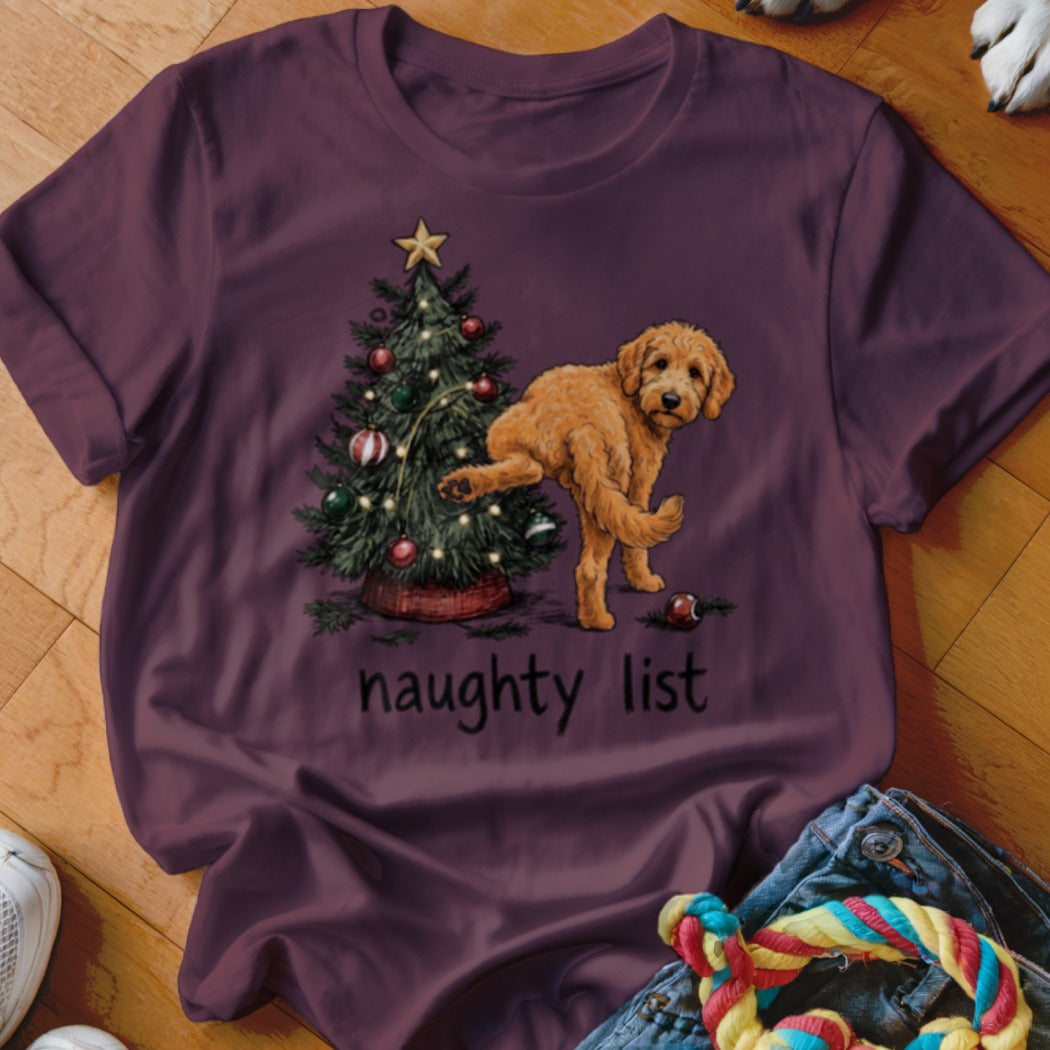 Dog next to Christmas tree with "naughty list" text on maroon t-shirt