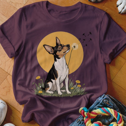 A plum-colored t-shirt displays an illustration of a black, white, and tan dog blowing dandelion seeds against a yellow moon.