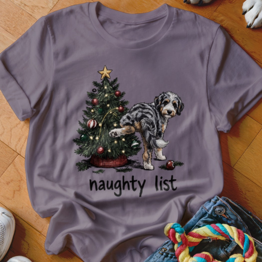 Dog lifting leg on Christmas tree with text "naughty list" on shirt.
