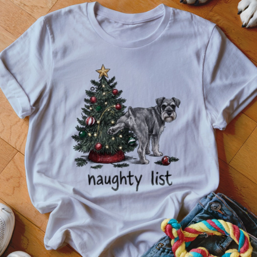 A white crewneck t-shirt featuring a graphic of a Schnauzer urinating on a Christmas tree with the text naughty list underneath.