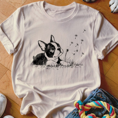 Light pink short-sleeved t-shirt featuring a black and white illustration of a dog in grass blowing dandelion seeds.