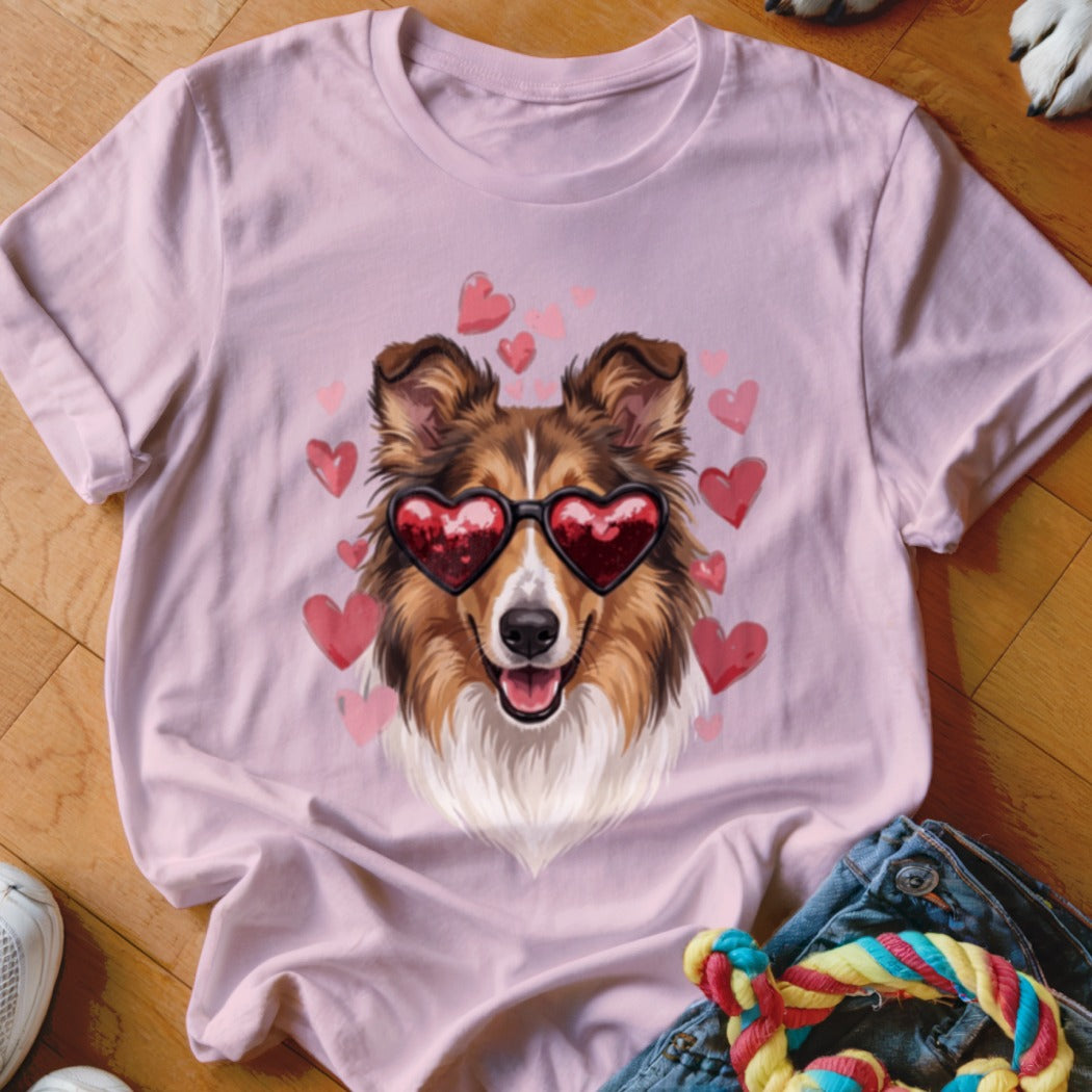 A light pink t-shirt features a graphic of a brown and white collie wearing heart-shaped sunglasses surrounded by pink hearts.