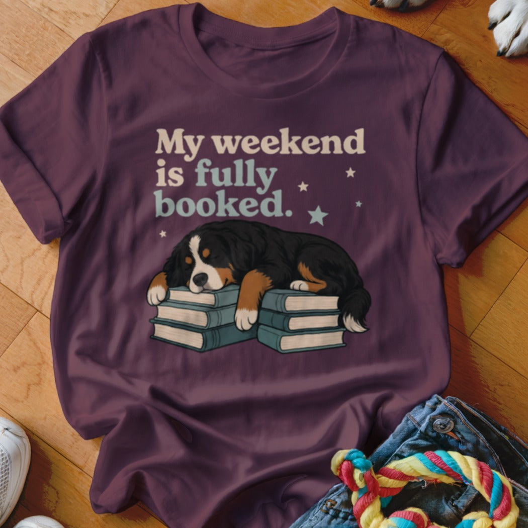 Bernese mountain dog sleeps on books with "My weekend is fully booked" text.