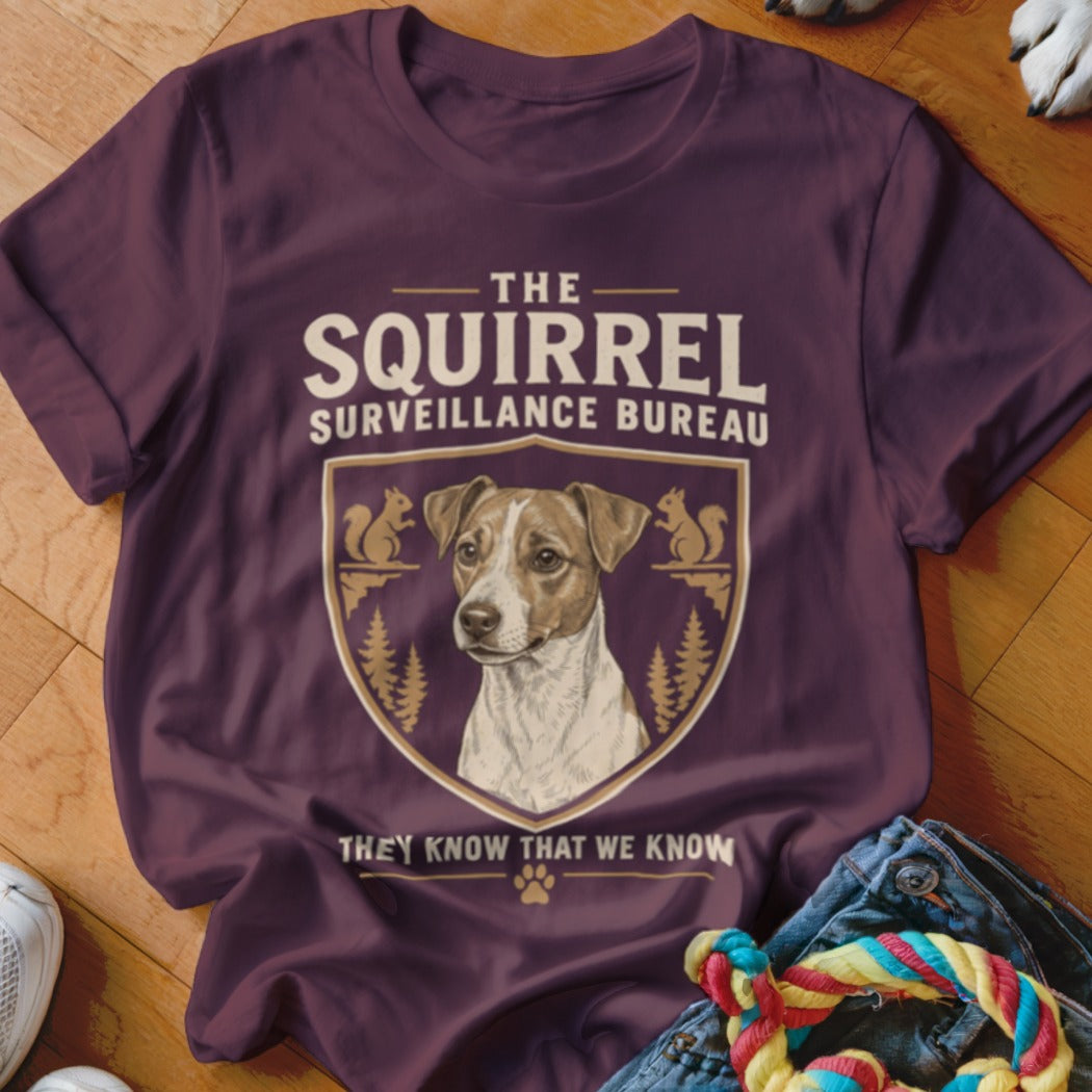 A dark plum t-shirt featuring a Jack Russell Terrier graphic and text reading The Squirrel Surveillance Bureau.
