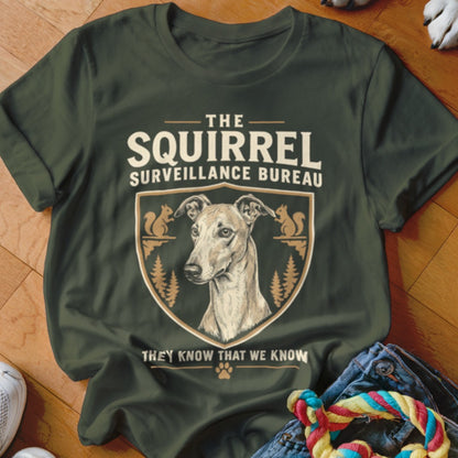 Dark green t-shirt with a vintage-style graphic featuring a dog, squirrels, trees, and text reading The Squirrel Surveillance Bureau.