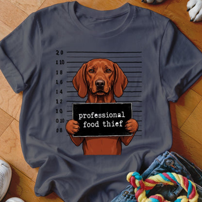 Brown dog holding a sign that says "professional food thief" in a mugshot background.