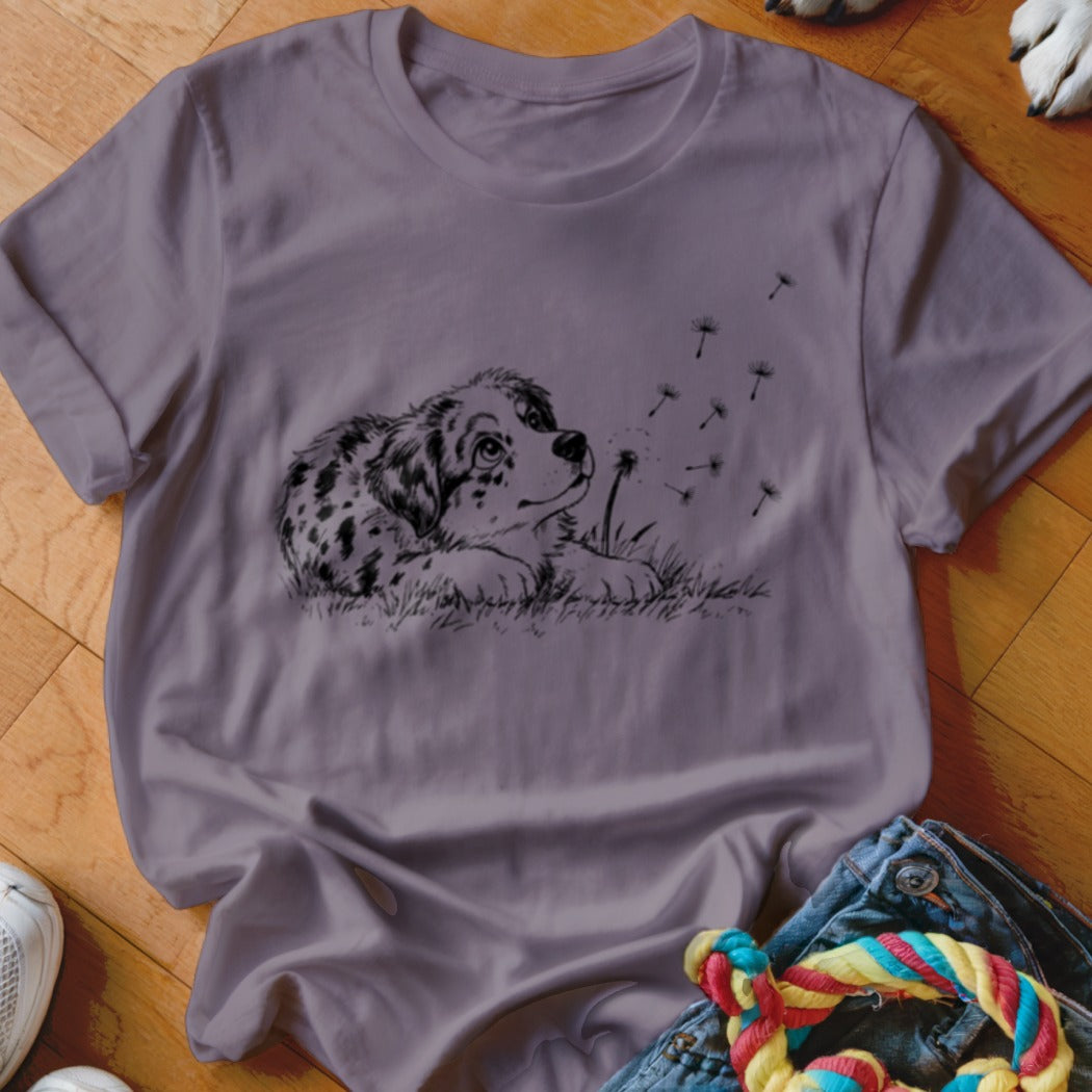 A purple crewneck t-shirt featuring a black line art graphic of a puppy blowing dandelions.