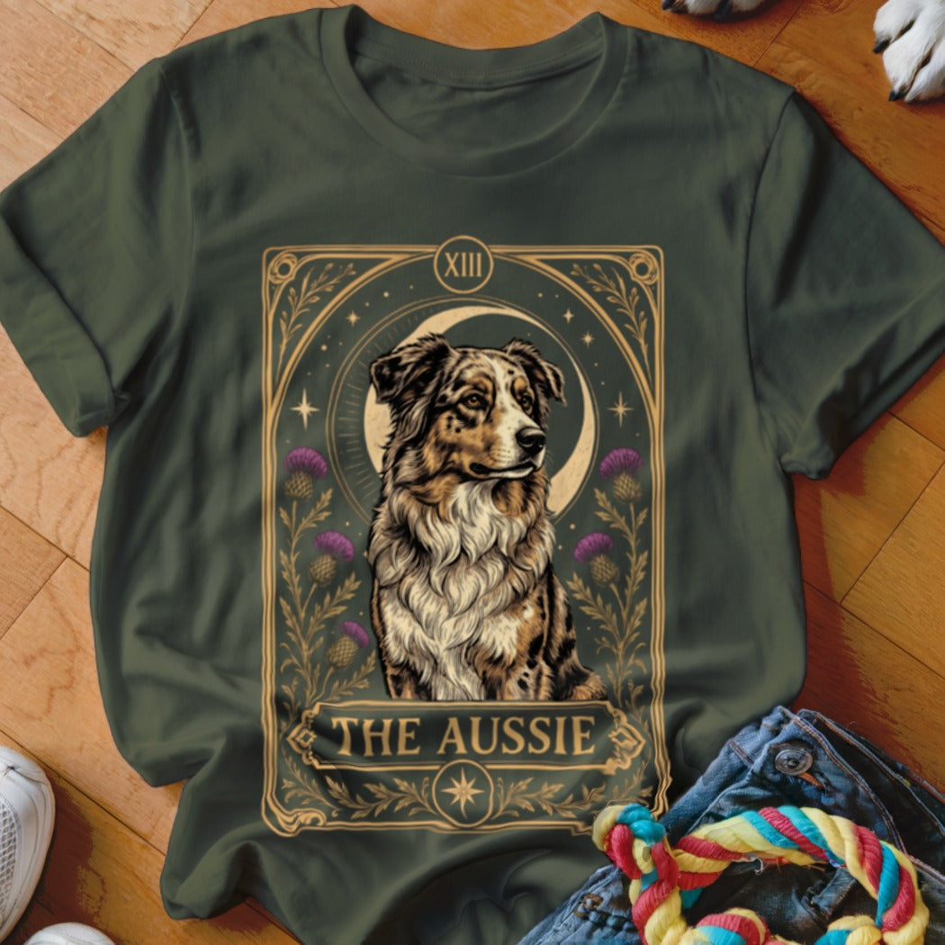 Dark green t-shirt featuring a tarot card style illustration of an Australian Shepherd with purple thistles and the text The Aussie.