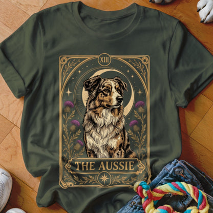Dark green t-shirt featuring a tarot card style illustration of an Australian Shepherd with purple thistles and the text The Aussie.