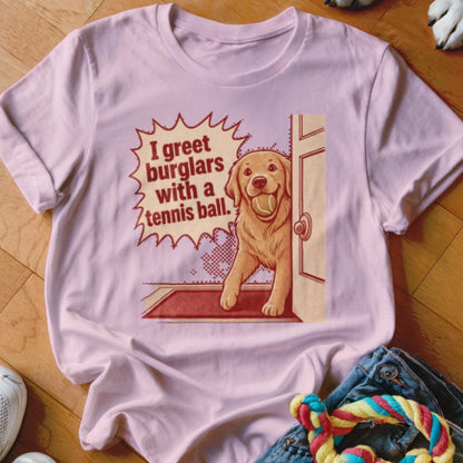 T-shirt graphic with text "I greet burglars with a tennis ball" and a golden retriever holding a tennis ball.