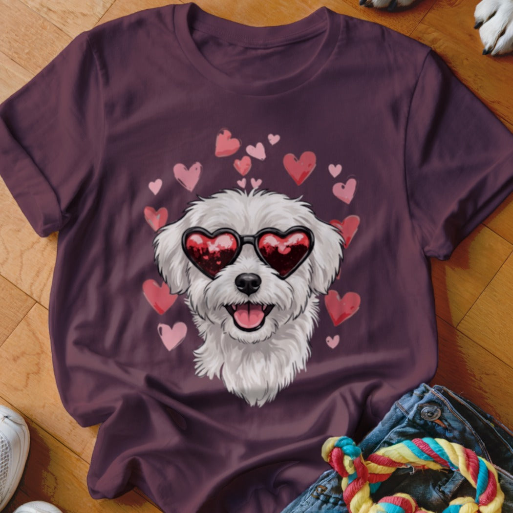 A dark purple t-shirt features a graphic of a white fluffy dog wearing heart-shaped sunglasses surrounded by pink hearts.