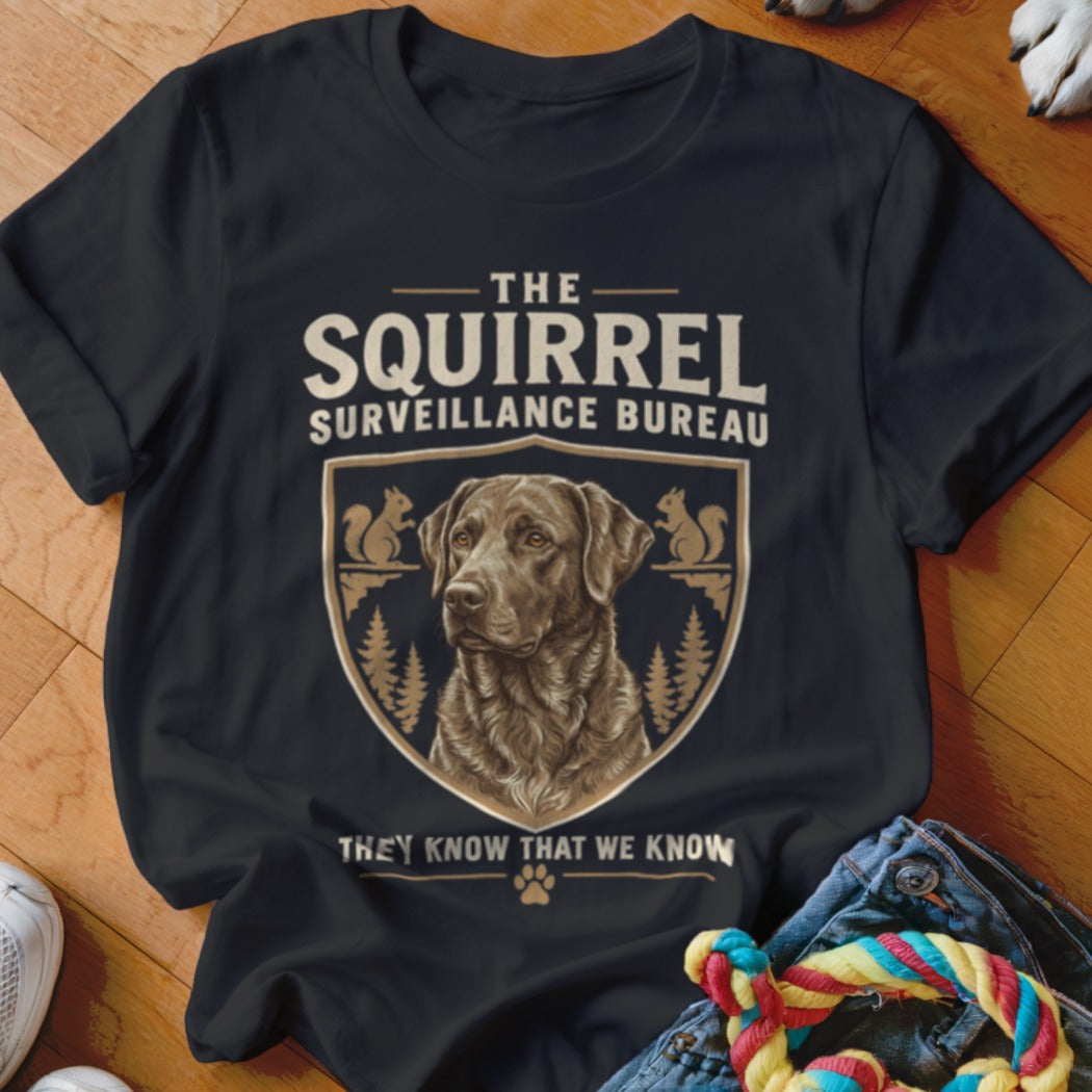Black t-shirt featuring a graphic design of a chocolate labrador inside a crest with squirrels and the text The Squirrel Surveillance Bureau.