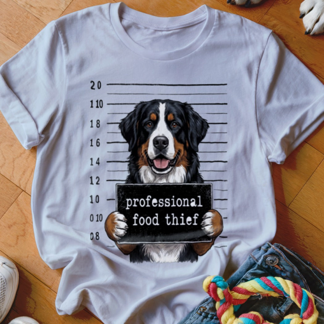 Bernese mountain dog mugshot with "professional food thief" sign on a white t-shirt.