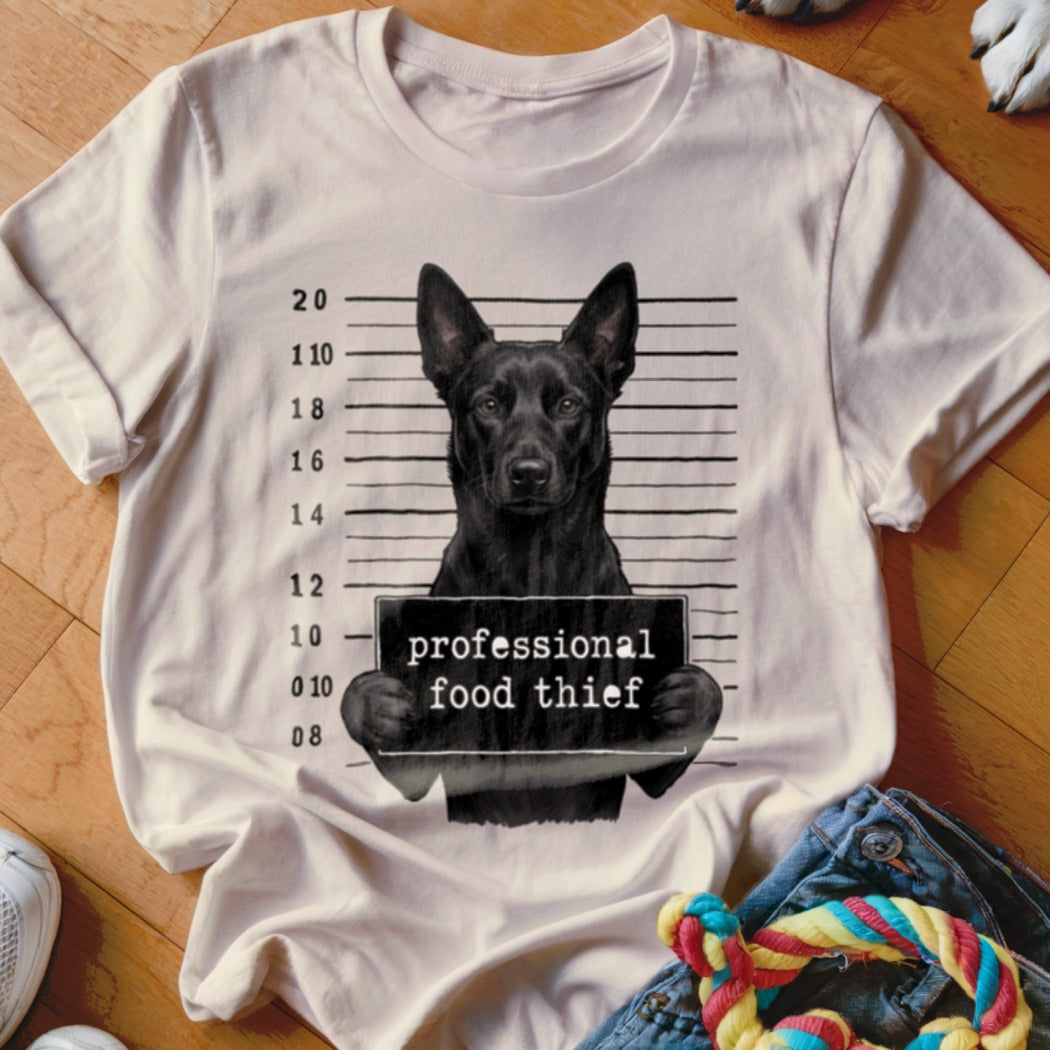 Black dog mugshot on a t-shirt reads "professional food thief."