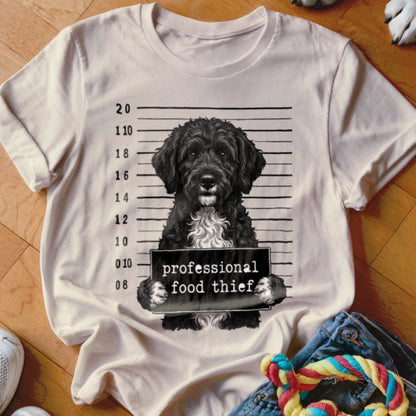 Black dog mugshot with "professional food thief" sign on a t-shirt.
