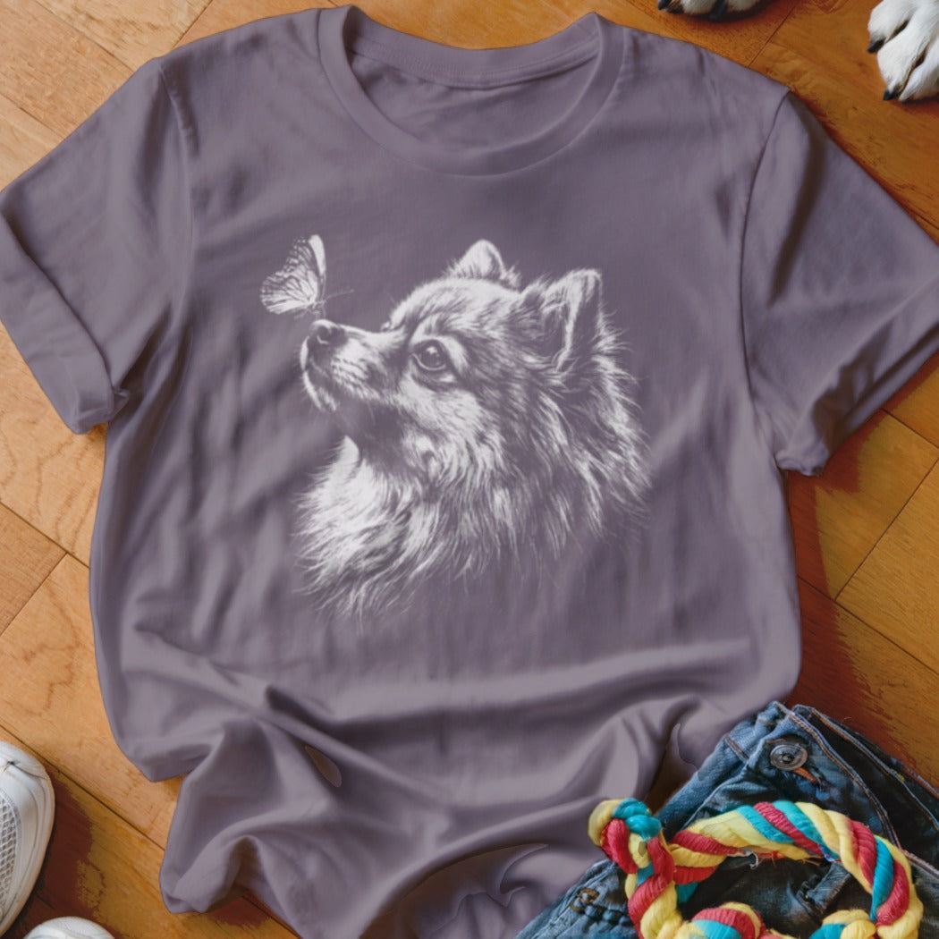 A purple crewneck t-shirt featuring a white graphic of a Pomeranian dog looking at a butterfly.