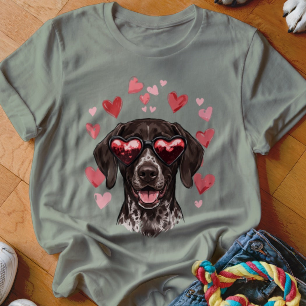 A sage green t-shirt featuring a graphic of a brown dog wearing heart-shaped sunglasses surrounded by floating pink hearts.