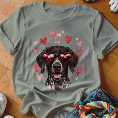 A sage green t-shirt featuring a graphic of a brown dog wearing heart-shaped sunglasses surrounded by floating pink hearts.
