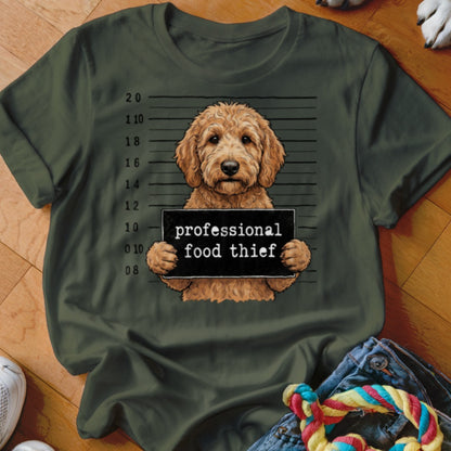 Goldendoodle dog mugshot with "professional food thief" sign on a green t-shirt.