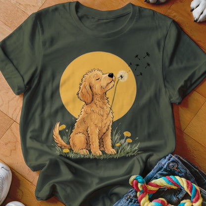 An olive green t-shirt featuring an illustration of a golden puppy blowing a dandelion against a yellow circle background.