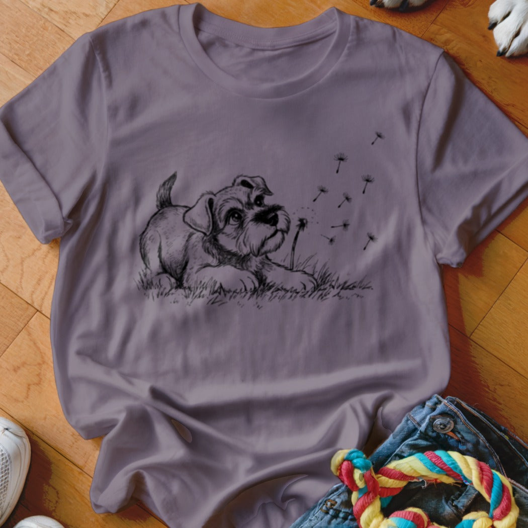 Dusty purple t-shirt featuring a black line drawing of a puppy watching blowing dandelion seeds.