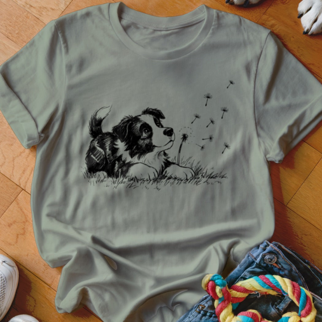 Sage green crewneck t-shirt featuring a black and white sketch of a puppy looking at blowing dandelion seeds.