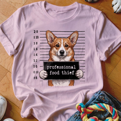 Corgi in mugshot holding "professional food thief" sign on pink t-shirt.