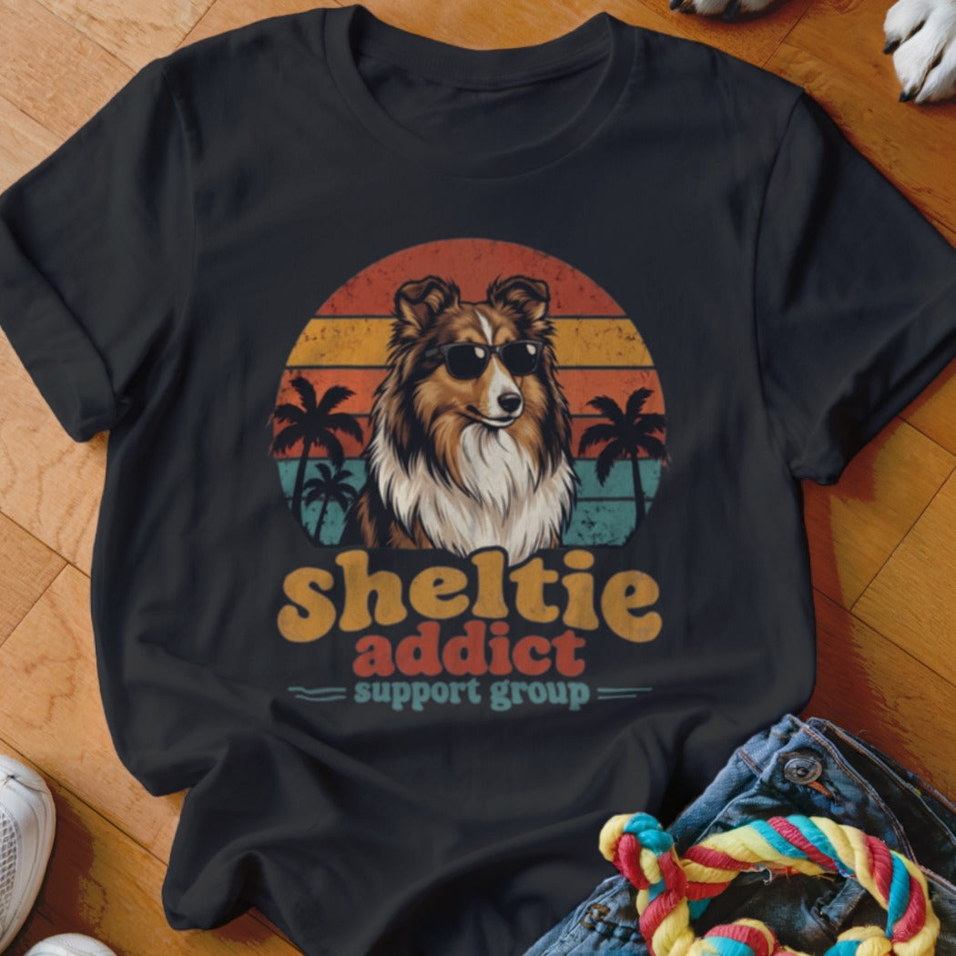 Black t-shirt featuring a retro graphic of a Shetland Sheepdog wearing sunglasses against a sunset and palm trees, with the text sheltie addict support group.