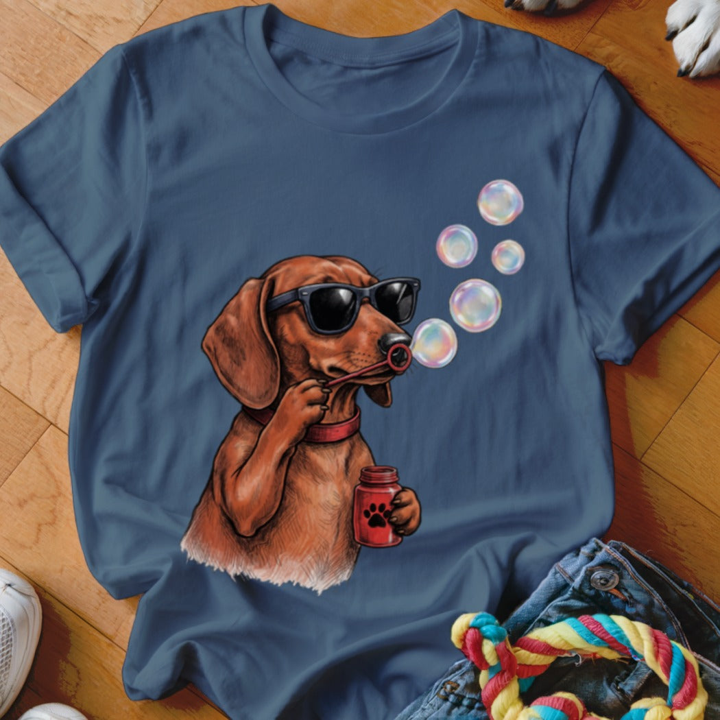 A dark blue t-shirt printed with a cartoon dachshund wearing sunglasses and blowing soap bubbles.
