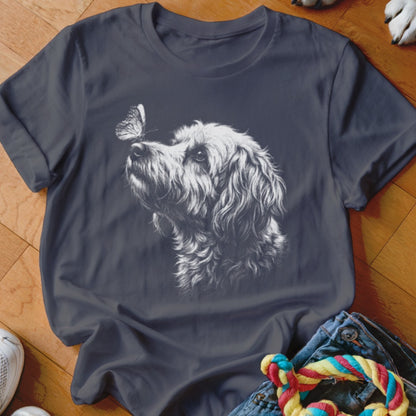 Dark gray short-sleeved t-shirt featuring a white sketched graphic of a fluffy dog looking at a butterfly on its nose.