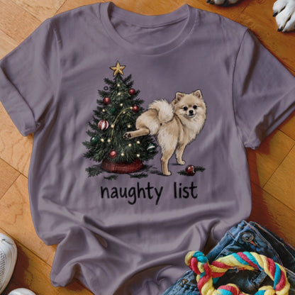 Pomeranian dog near Christmas tree with text "naughty list" on shirt.