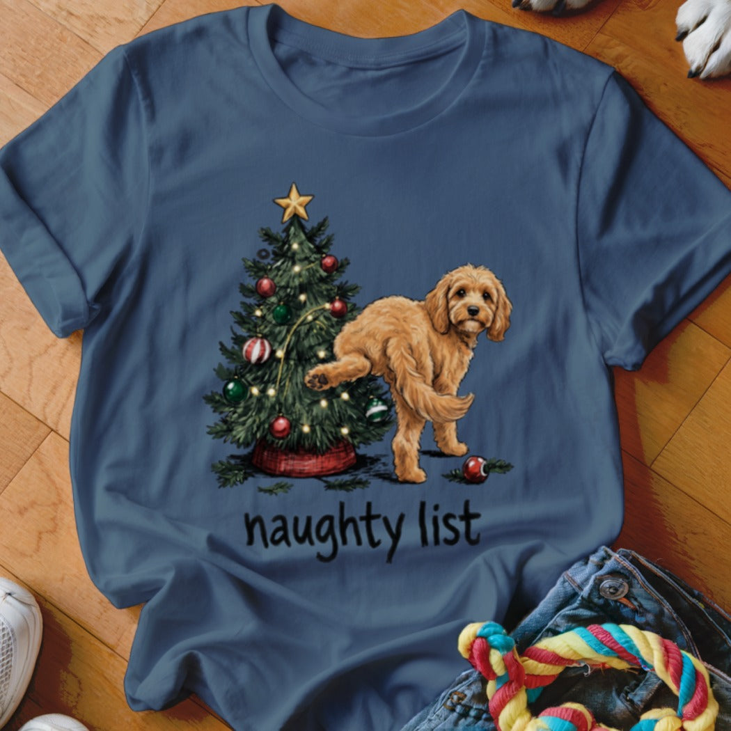 A golden doodle dog lifts its leg by a decorated Christmas tree with the text "naughty list".