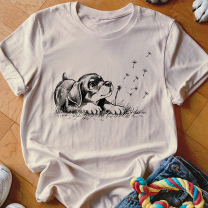 A light-colored t-shirt features a black line drawing of a puppy looking up at dandelion seeds.