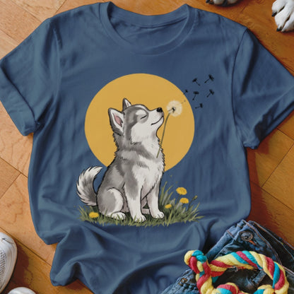A blue t-shirt featuring an illustration of a husky puppy blowing a dandelion against a yellow circle.