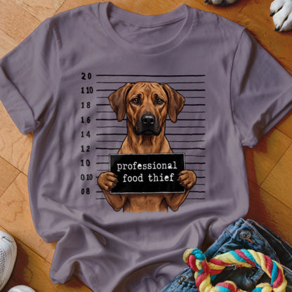 Rhodesian Ridgeback mugshot with "professional food thief" sign on a purple t-shirt.