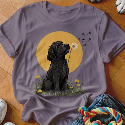 A grey short-sleeved t-shirt featuring a graphic of a black dog blowing a dandelion against a yellow circle background.