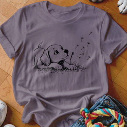 A mauve crewneck t-shirt featuring a black line art graphic of a puppy blowing dandelion seeds.