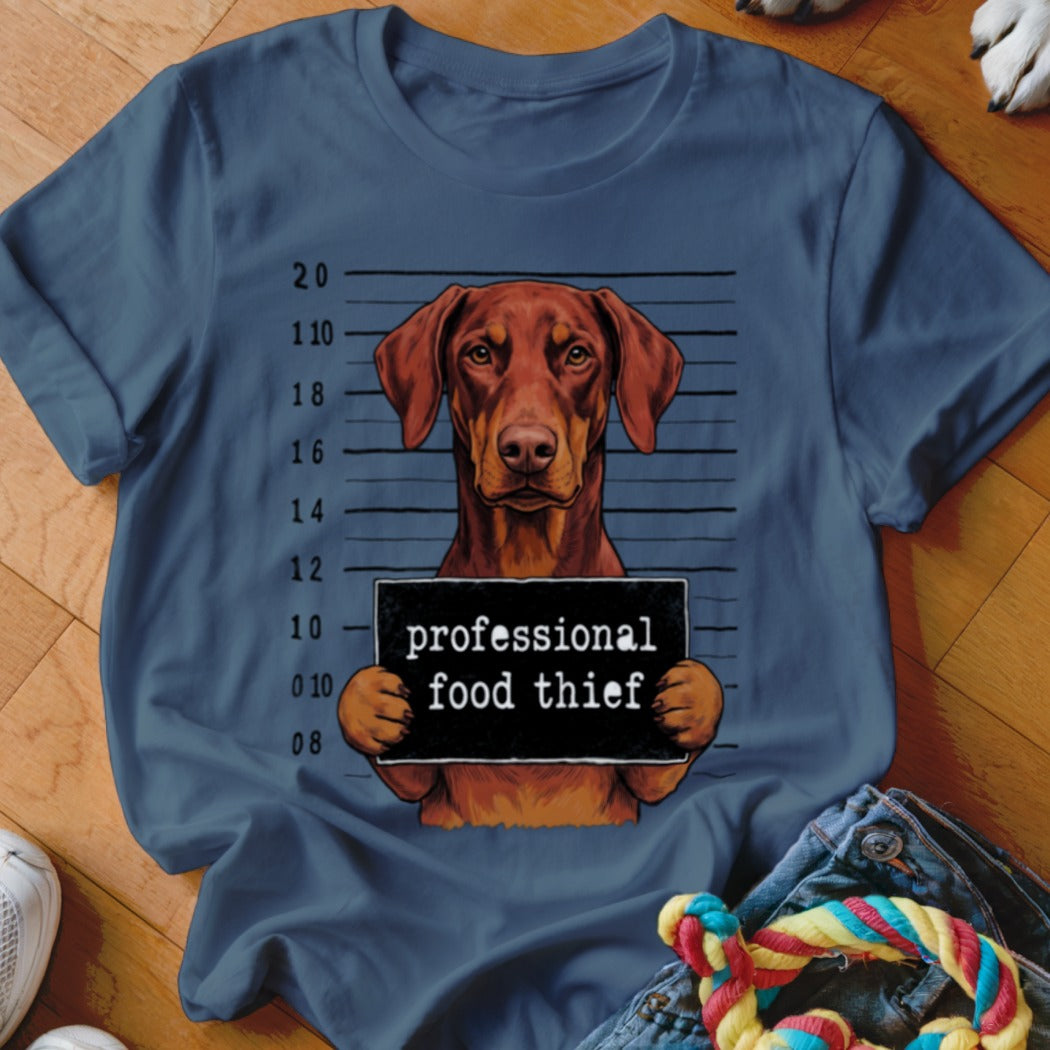 Brown dog in mugshot holding a "professional food thief" sign.