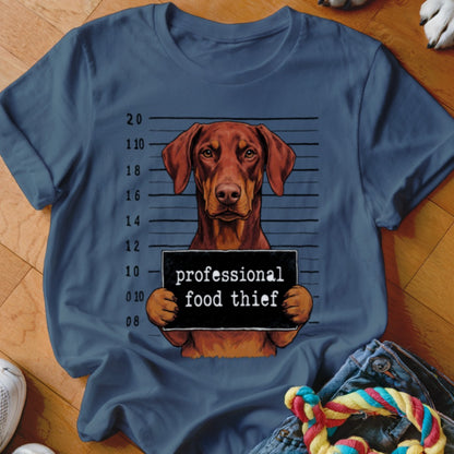 Brown dog in mugshot holding a "professional food thief" sign.