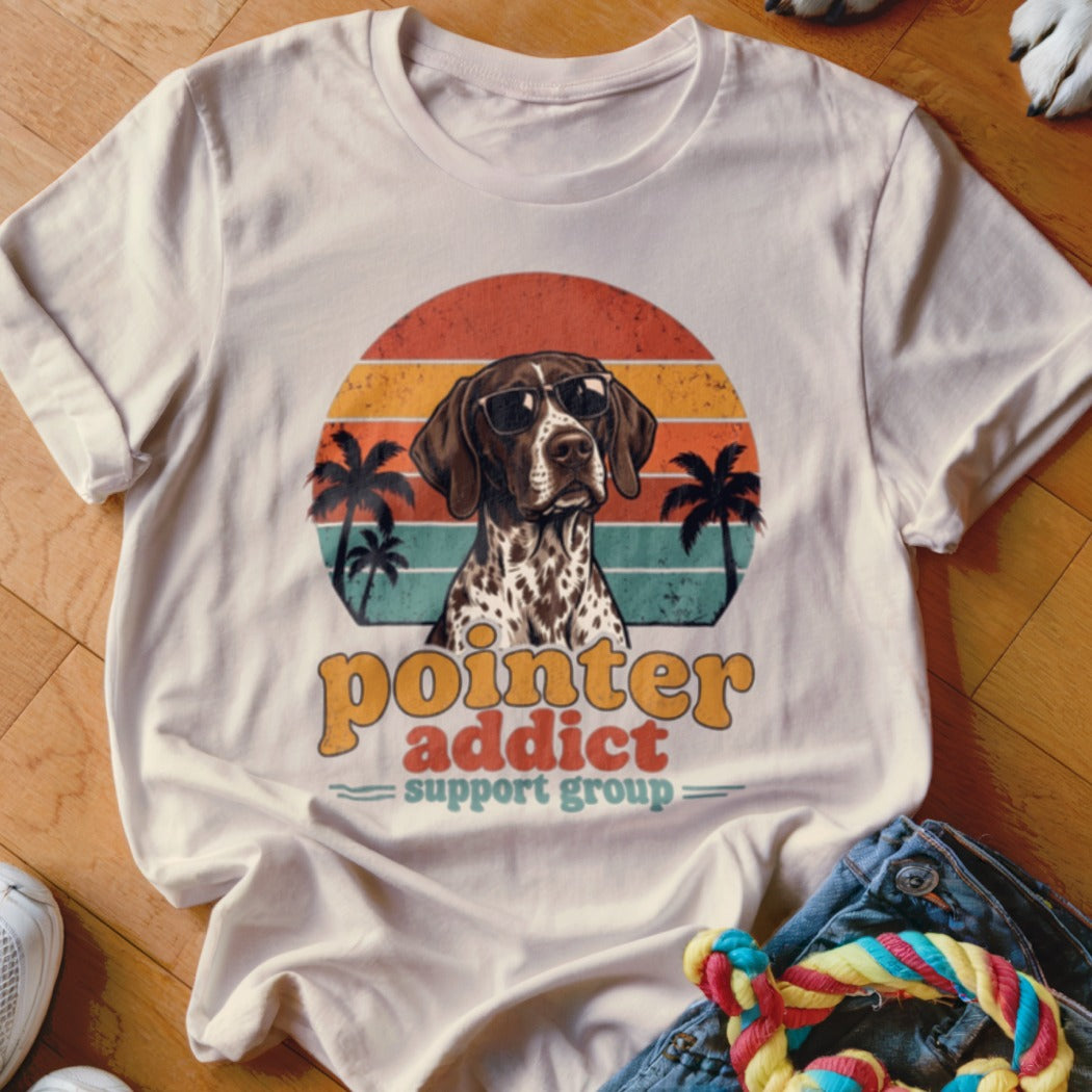 Beige t-shirt featuring a graphic of a German Shorthaired Pointer wearing sunglasses against a retro sunset and palm tree background, with text reading Pointer Addict Support Group.