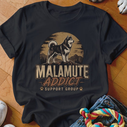 Black crewneck t-shirt featuring a vintage-style graphic of a malamute standing before a sun and mountains, with text reading "Malamute Addict Support Group."