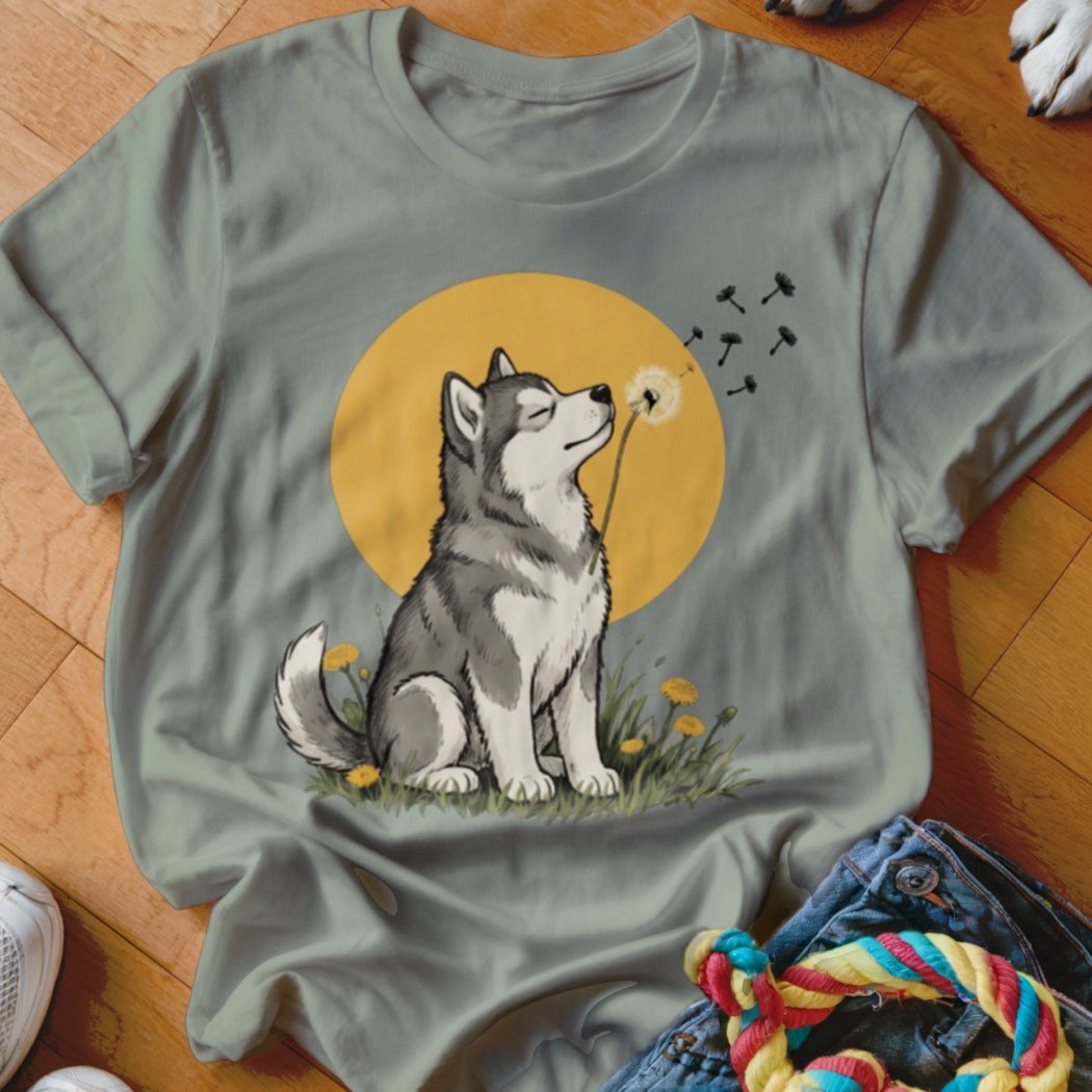 Sage green t-shirt featuring an illustrated husky blowing dandelion seeds against a yellow sun background.