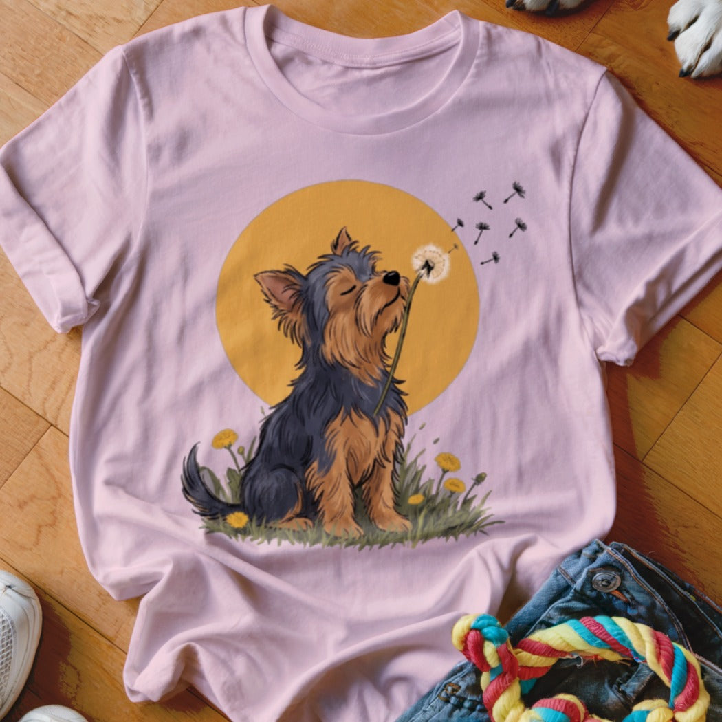 A light pink t-shirt featuring an illustration of a Yorkshire terrier blowing a dandelion against a yellow circle background.